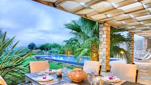 A dining area with a view of a pool and palm trees. - Cretan Mansion with Heated Swimming Pool (Apokoronas)