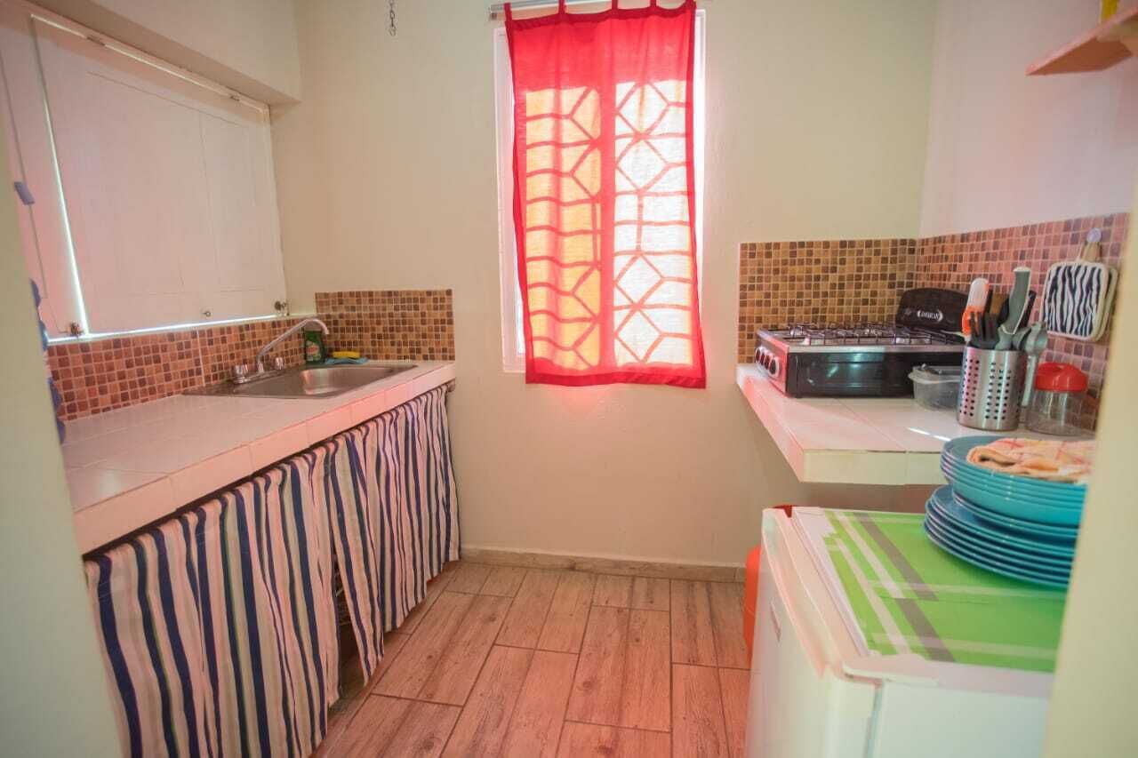 Et kompakt køkken med flisebeklædt væg, gasblus, vask og et vindue med rødt gardin.