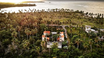 Vista aérea de una zona costera con un grupo de edificios rodeados de palmeras y una playa.