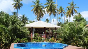 A hot tub surrounded by tropical plants and palm trees, with a covered seating area in the background. - 21 Palms (Las Galeras)