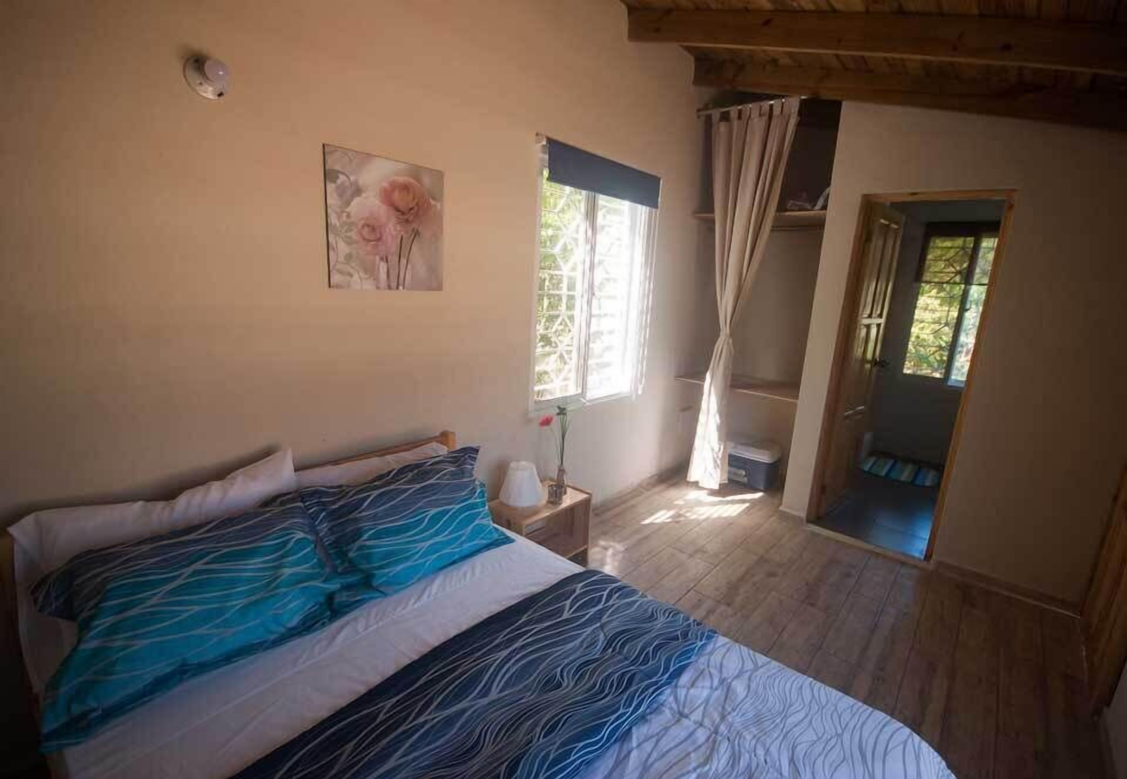 A bedroom with a bed, a painting, a window with curtains, and a door leading to another room.