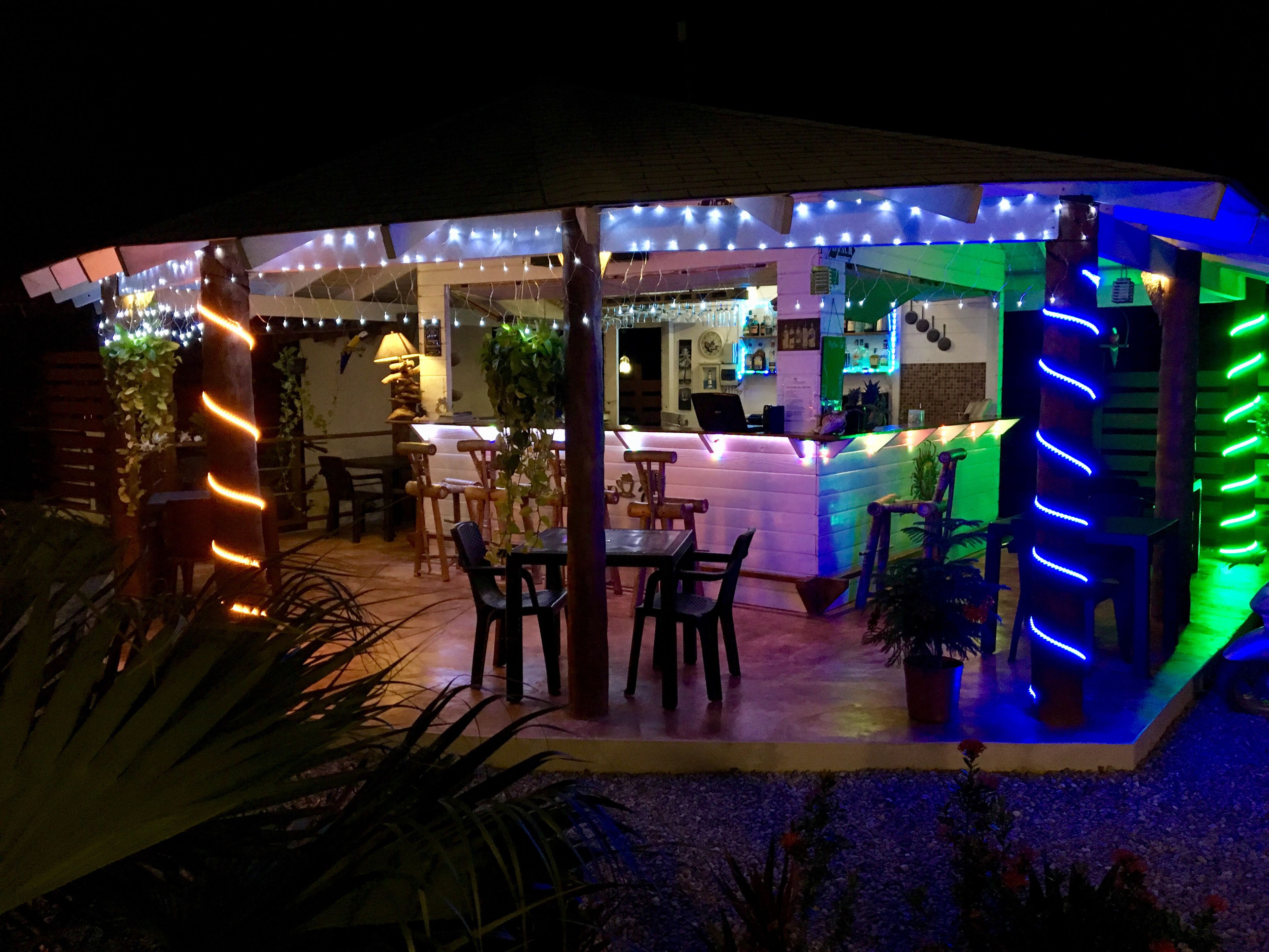 An outdoor seating area with tables and chairs, a bar area with a counter, and string lights.