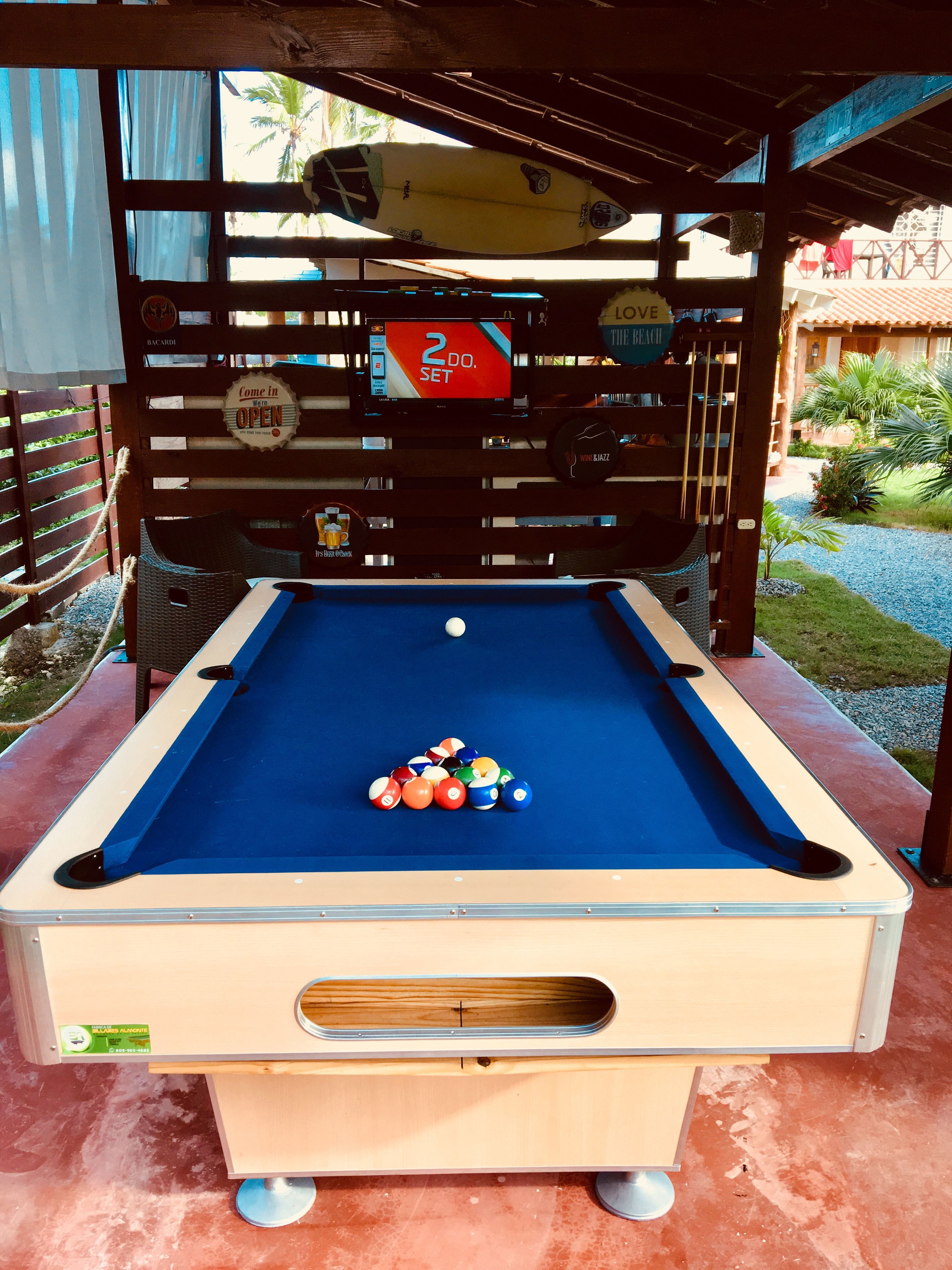 Una mesa de billar con superficie de fieltro azul, rodeada por una estructura de madera con un letrero que indica una oferta de 2 DÓLARES.