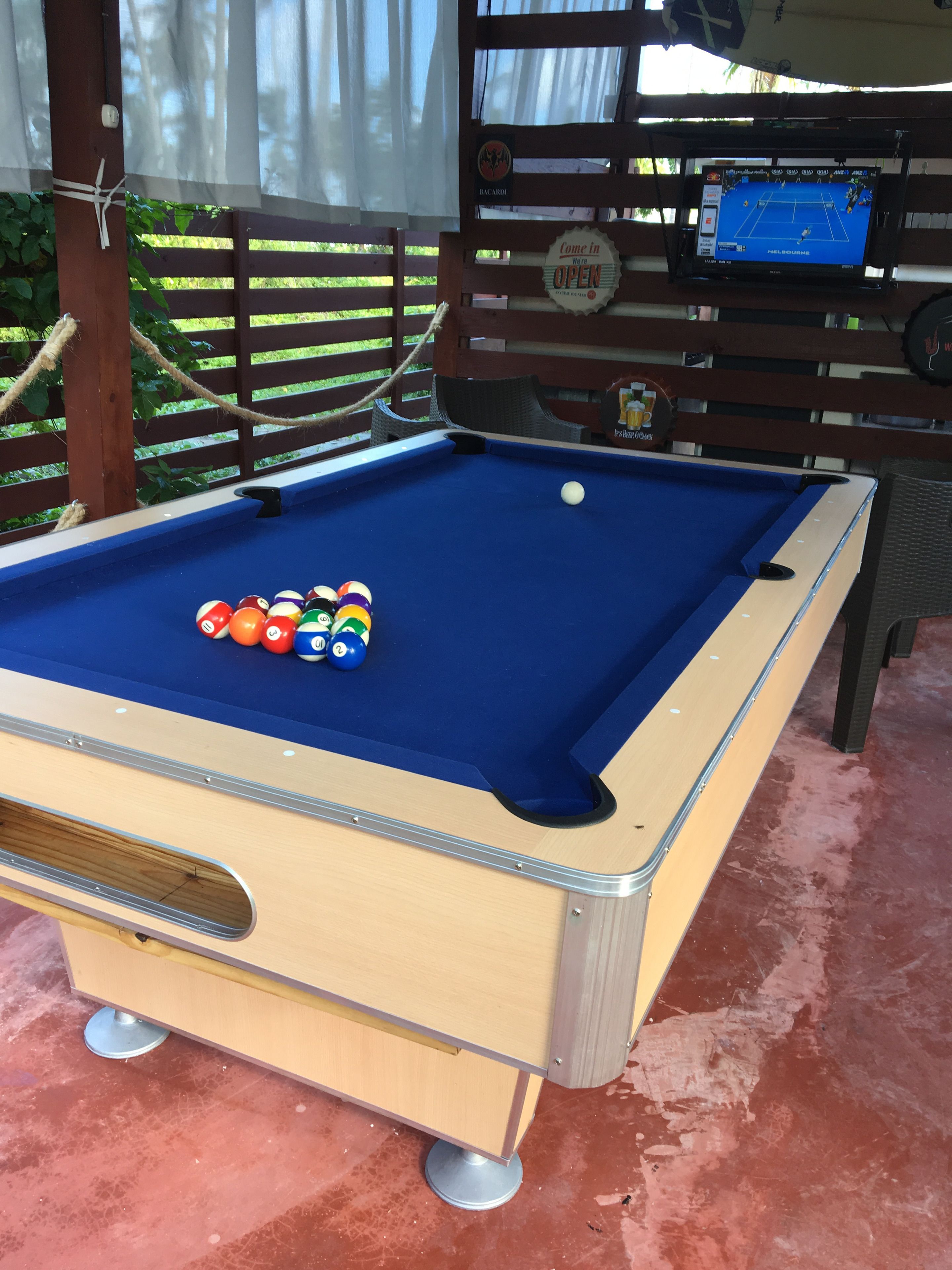 A pool table with balls, a wooden table, and a screen displaying a game.