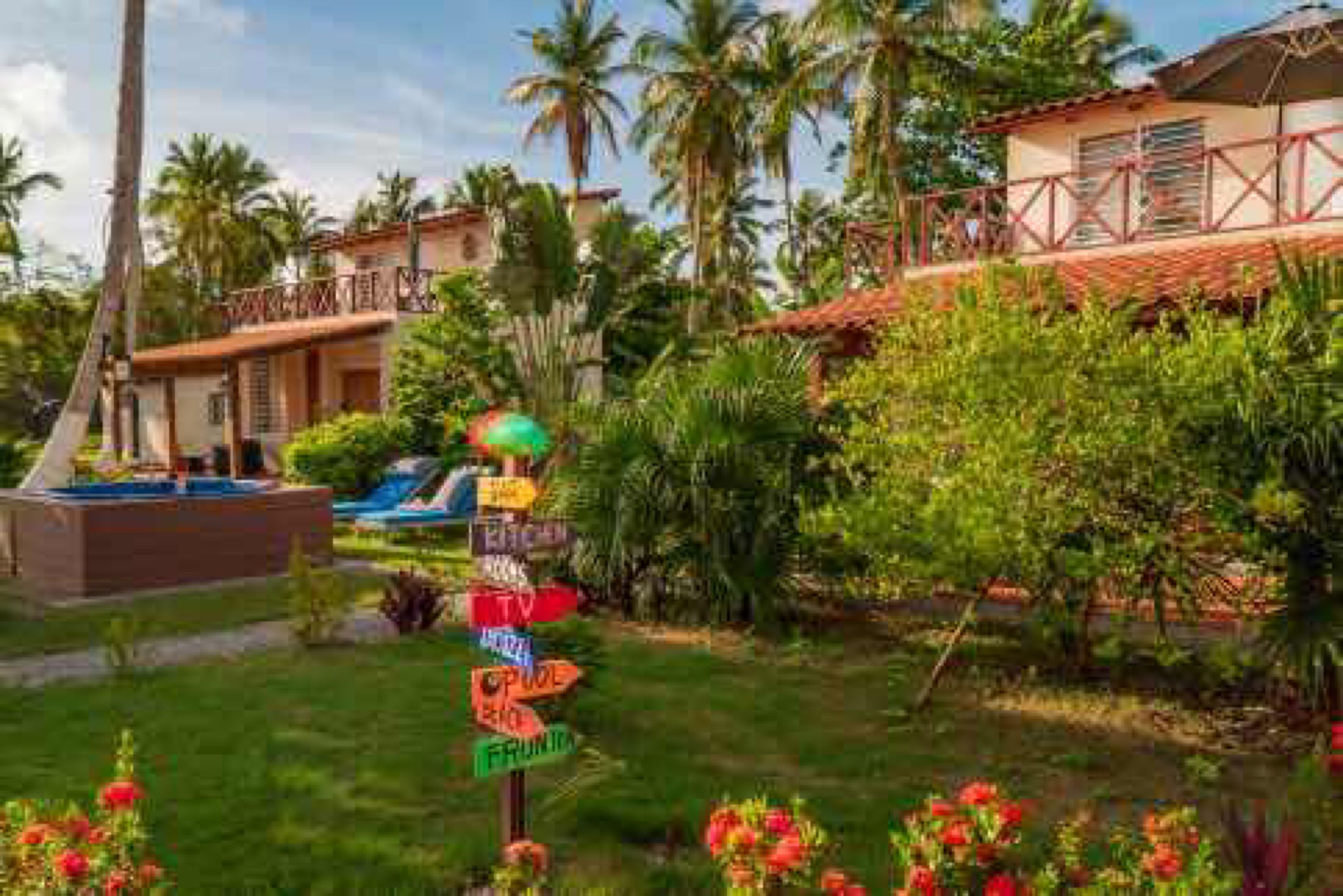 A tropical resort with a pool, palm trees, and a signpost with various amenities.