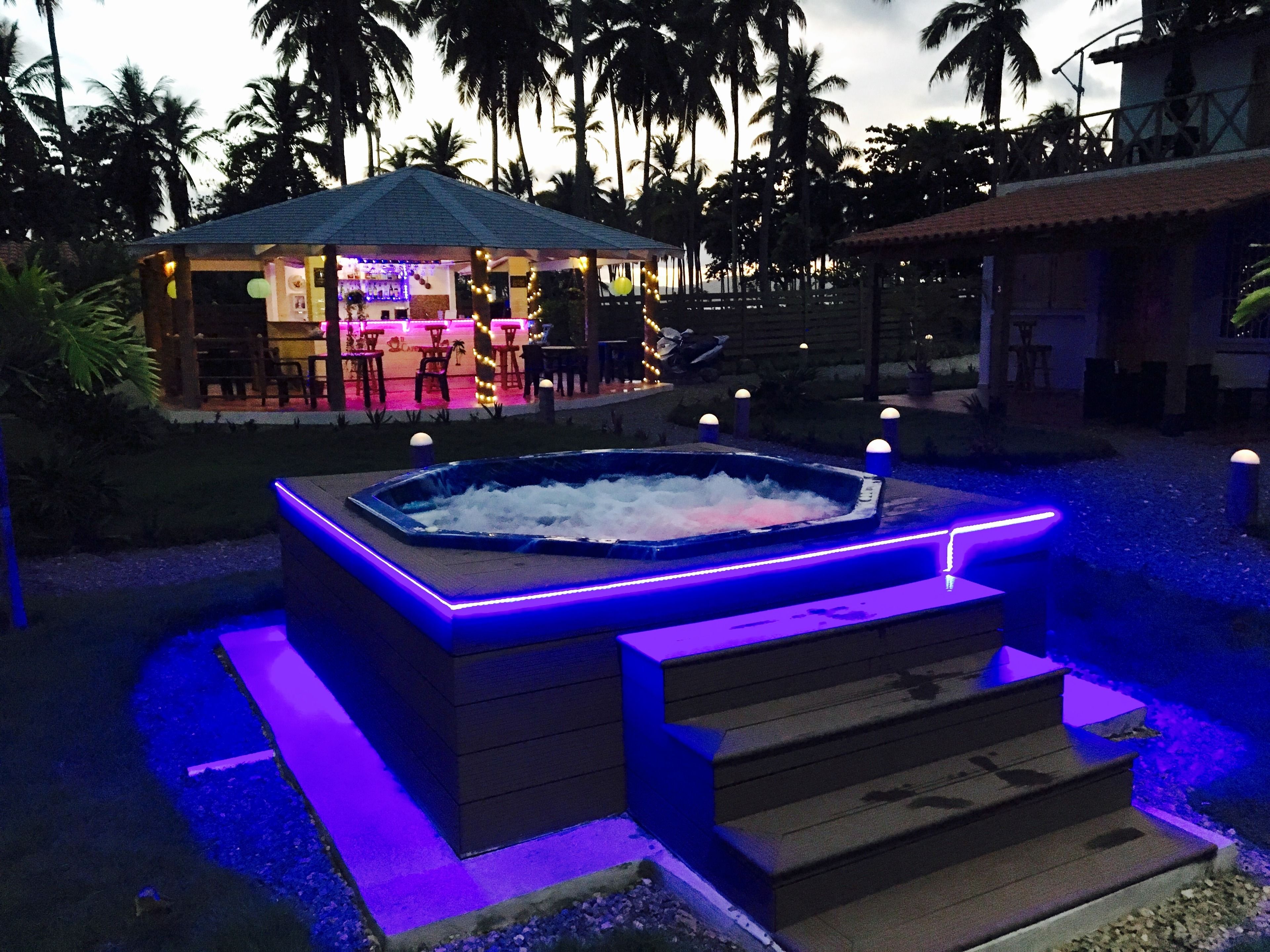 A hot tub with steps and LED lighting, surrounded by palm trees and a bar area with outdoor seating.