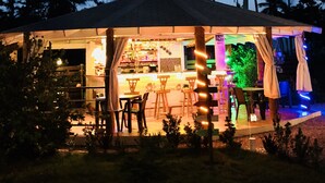 A cozy outdoor seating area with tables and chairs, surrounded by palm trees under a clear sky. - 21 Palms (Las Galeras)