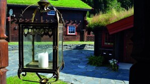 A rustic wooden house with a stone pathway leading to it, surrounded by greenery and a small garden.