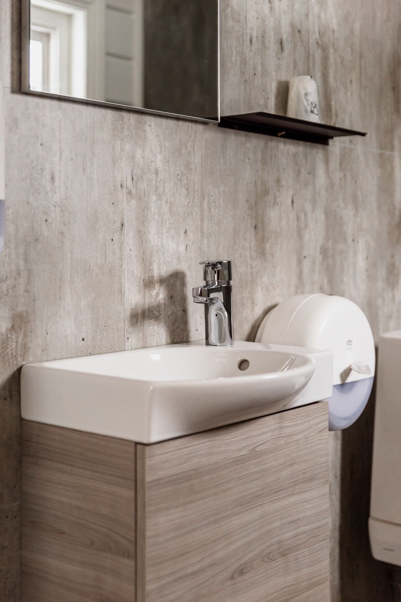 Un bagno con lavandino bianco, uno specchio ed un distributore di asciugamani.