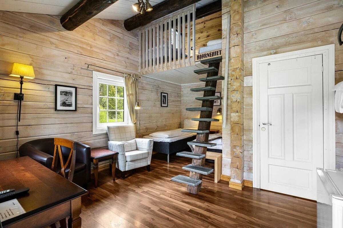 A wooden cabin interior with a dining area, a staircase, and a bed.