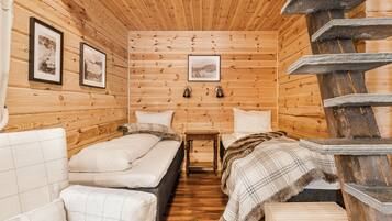 A cabin-style room with wooden walls and floors, two beds, a small table, and a wooden staircase.