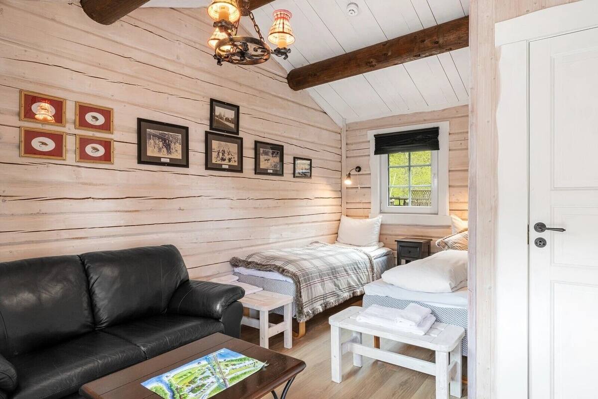 A cozy room with a wooden ceiling, a black leather sofa, a bed with a plaid blanket, and a small table with a book.