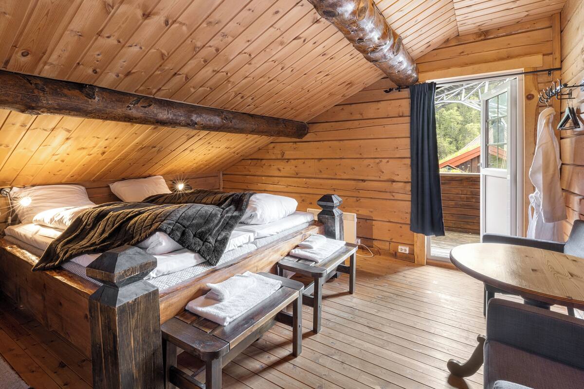 A wooden cabin bedroom with a bed, bench, and table.