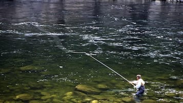 A person fishing in a clear river with visible rocks.