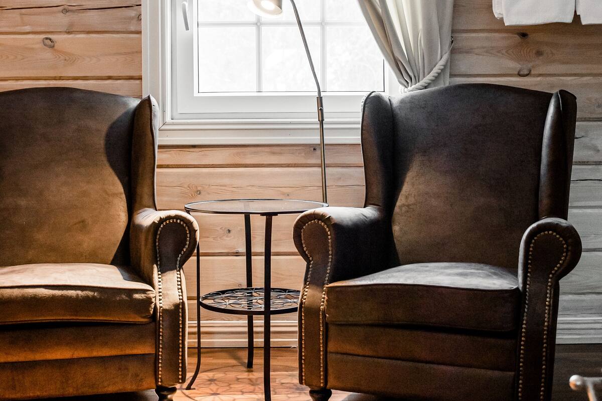 A room with two leather armchairs, a small round table, a floor lamp, and a window with curtains.
