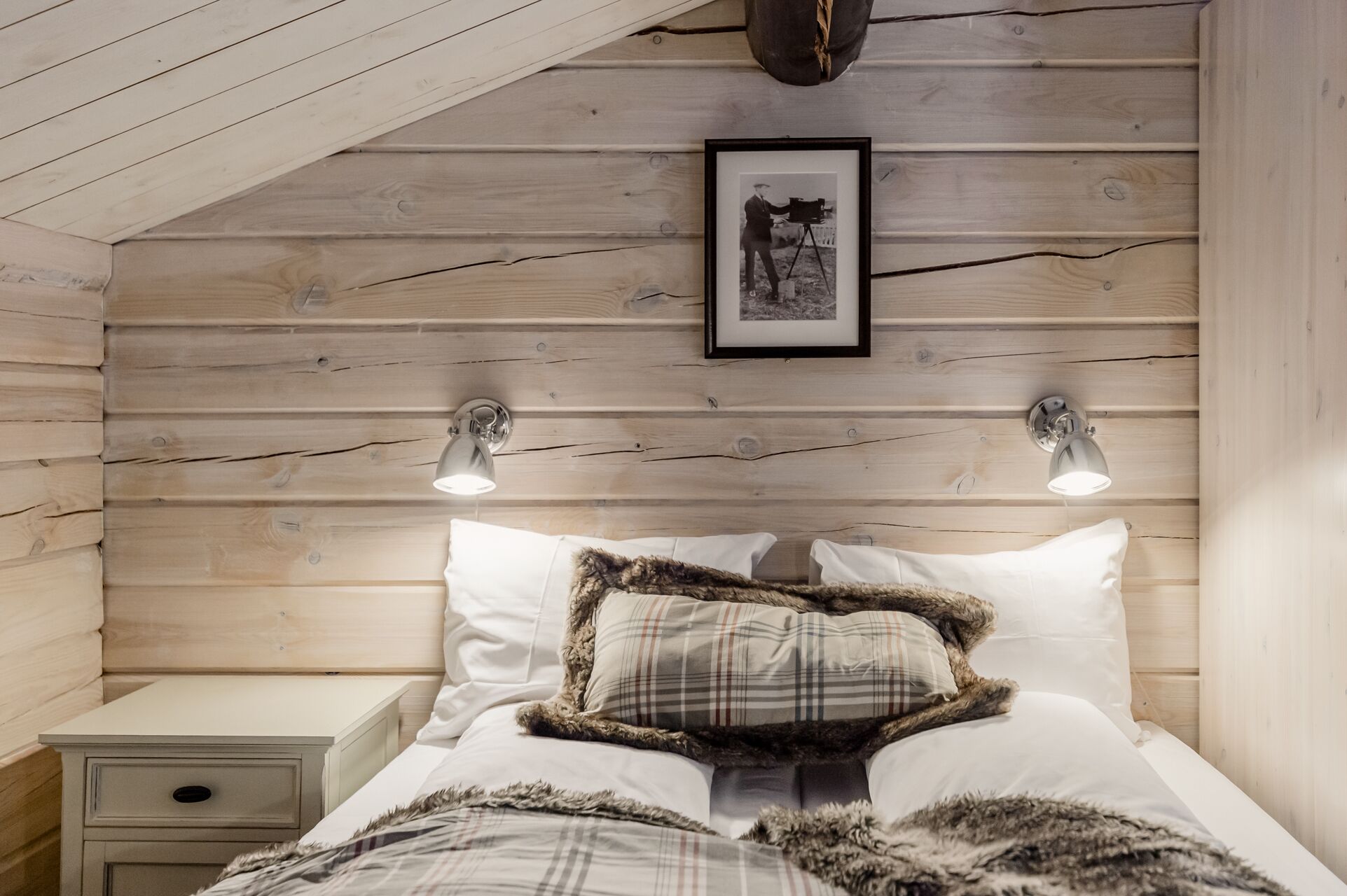 Um quarto aconchegante com teto de madeira, um quadro emoldurado, duas luminárias de cabeceira e uma cama com vários travesseiros.