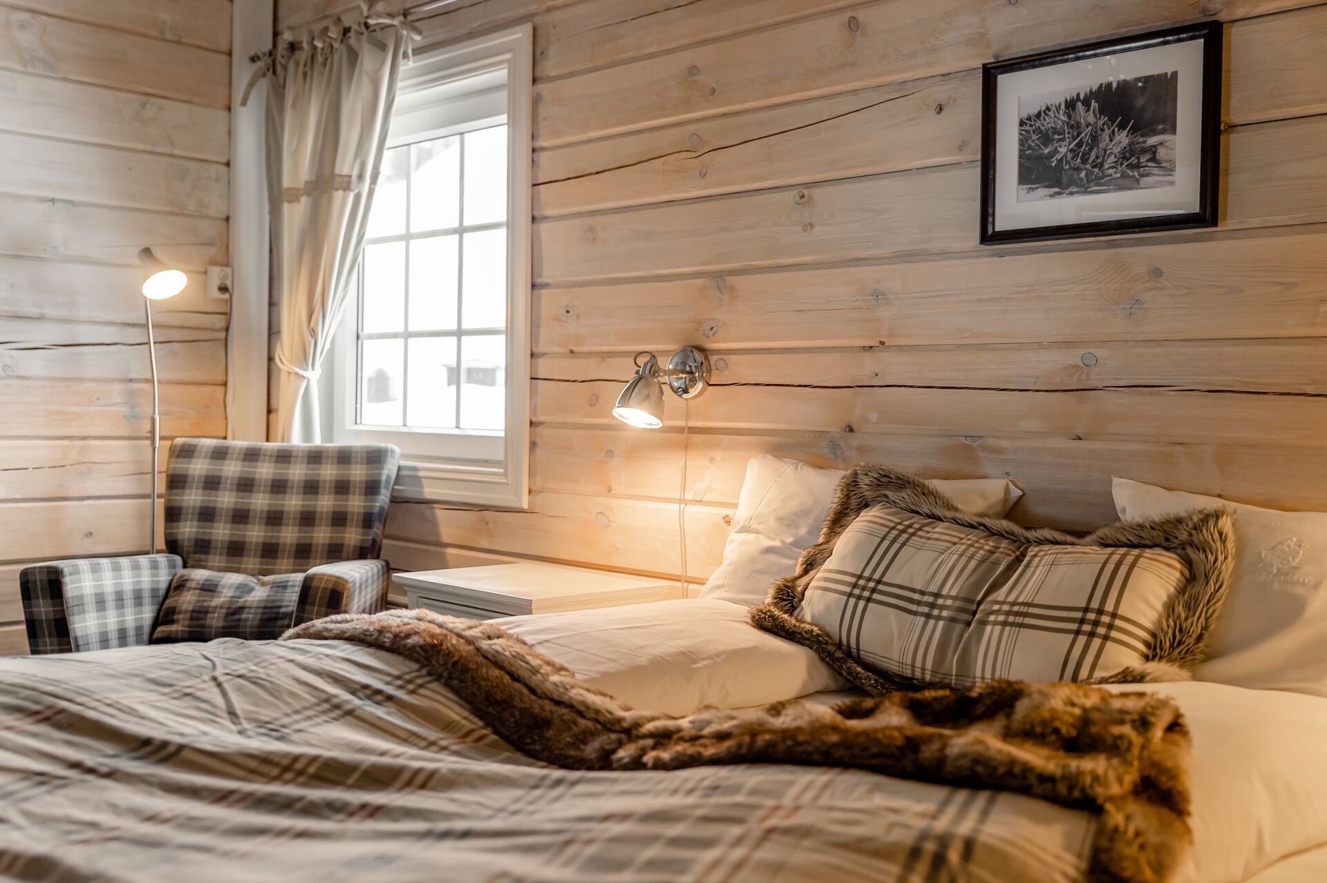 A cozy bedroom with a bed, a chair, a bedside table, a lamp, and a window with curtains.