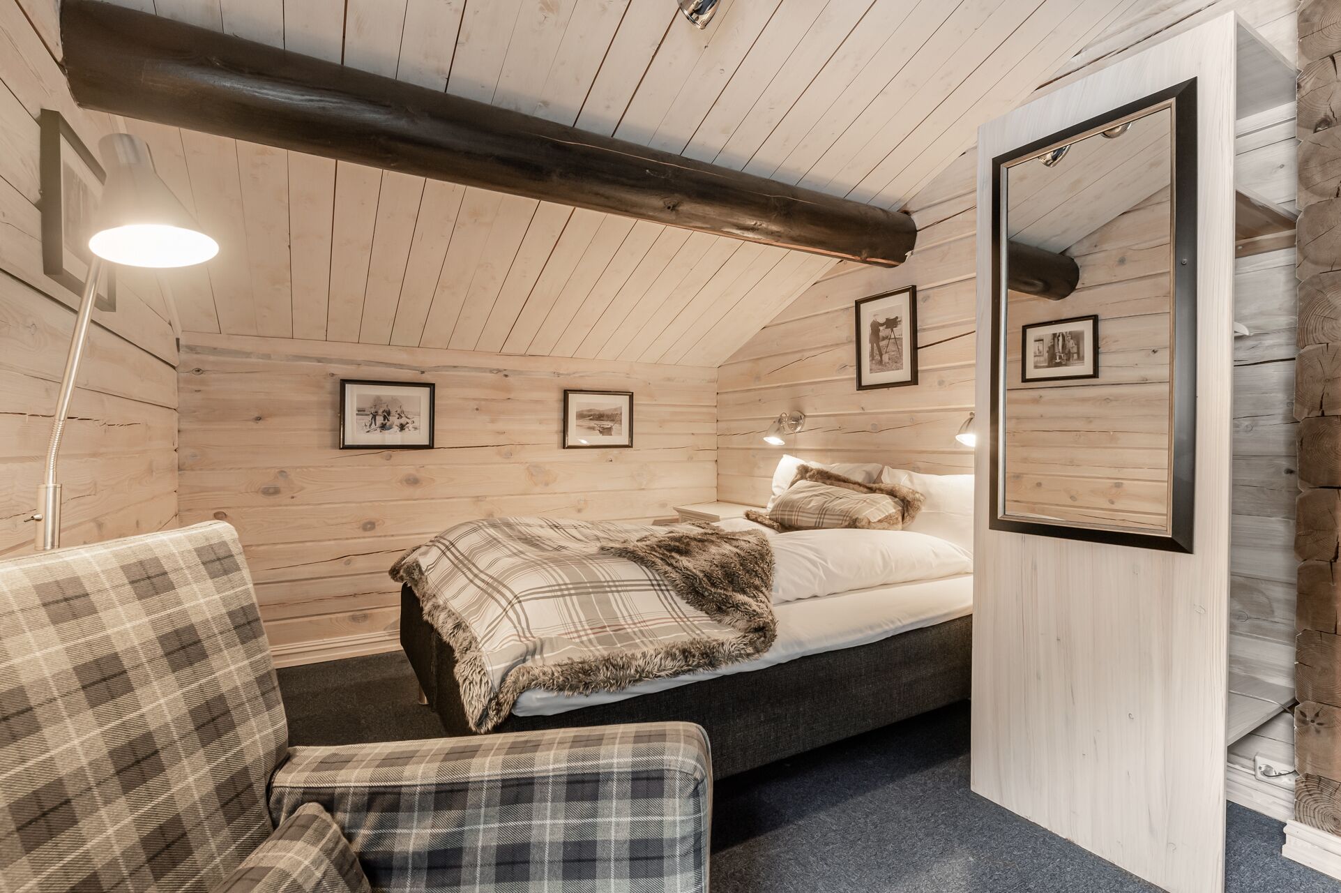 Een knus houten blokhuttenkamer met een bed, een stoel en ingelijste foto’s aan de wanden.