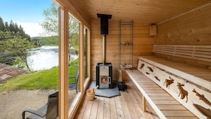A wooden cabin with a fireplace, large windows overlooking a river, and a deck with animal carvings.