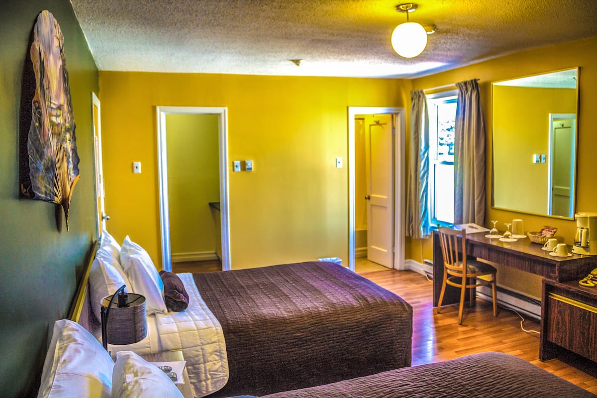 Une chambre avec deux lits, un bureau et une chaise. Il y a un miroir au mur et une fenêtre avec des rideaux.