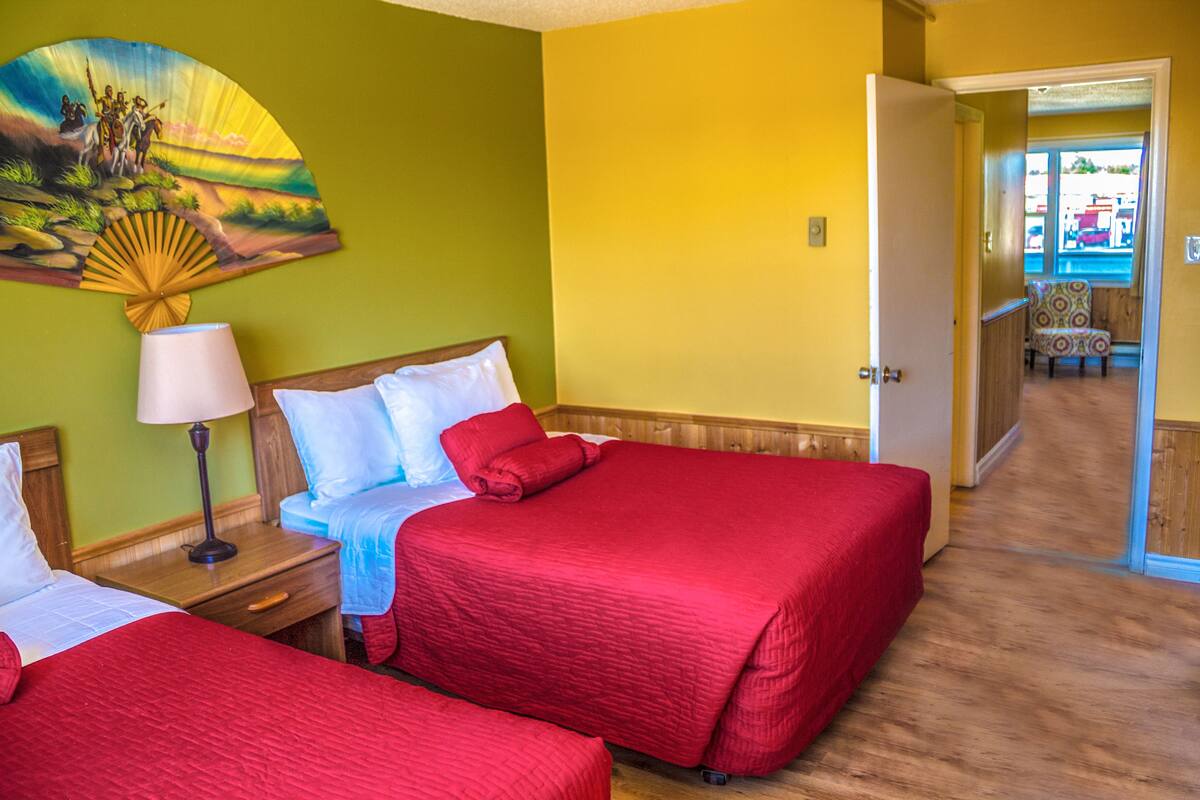 Une chambre d’hôtel avec deux lits, une table de chevet avec une lampe, un tableau au mur et une vue sur la piscine.