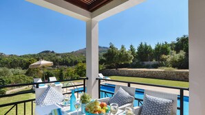 A terrace with a pool, dining table with chairs, and a view of the surrounding landscape. - Seven Springs Villas (Rhodes)