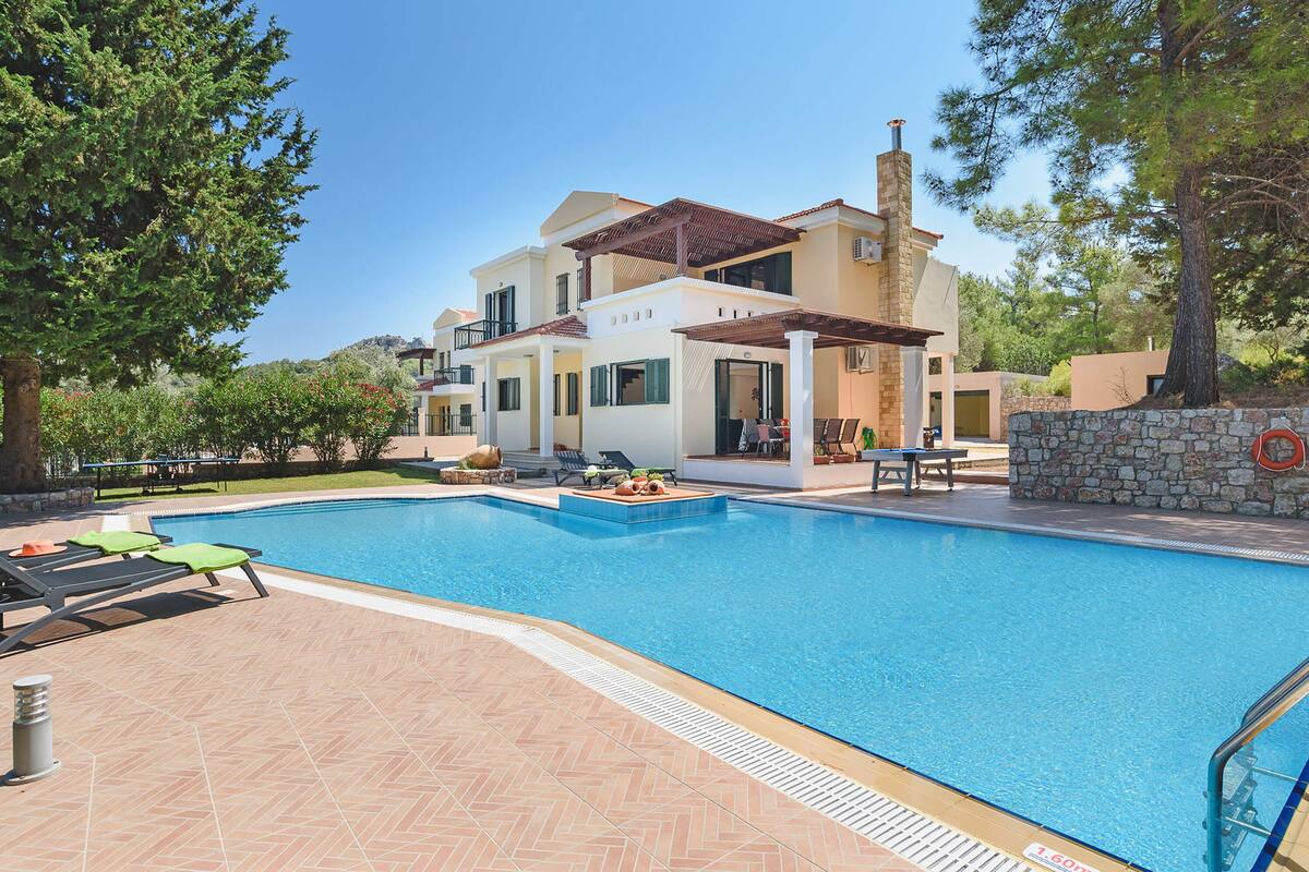 A modern two-story house with a swimming pool, outdoor furniture, and a stone wall.