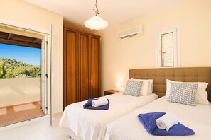 A bedroom with two beds, a wooden wardrobe, an air conditioning unit, and a balcony with a view.