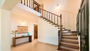 A spacious hallway with a wooden staircase, a bench, and a framed map on the wall. - Seven Springs Villas (Rhodes)