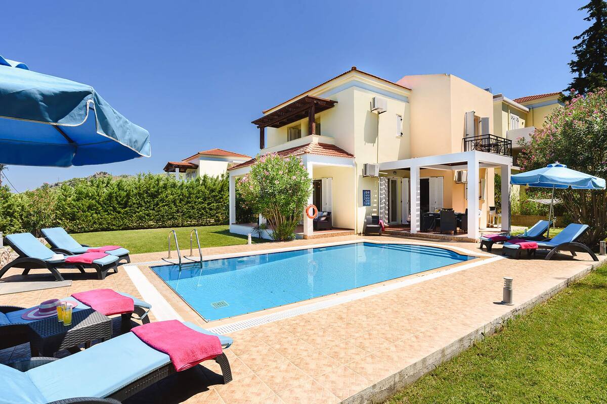 A swimming pool with lounge chairs and umbrellas, surrounded by a building with a balcony.