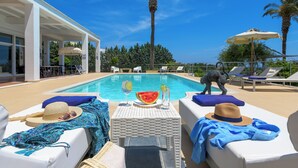 A poolside area with lounge chairs, a table with a watermelon and drinks, and a statue. - Grande Dame Villa of Rhodes (Rhodes)