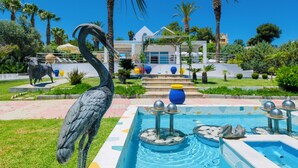 A pool area with a fountain, palm trees, and a statue of a bird. - Grande Dame Villa of Rhodes (Rhodes)