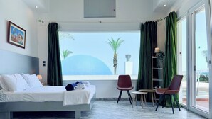 A hotel room with a bed, a chair, a small table, and a view of the sea. - Grande Dame Villa of Rhodes (Rhodes)
