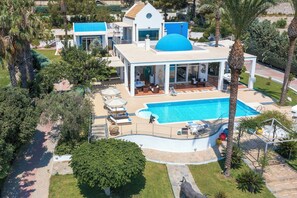 Et moderne hus med en stor swimmingpool, omgivet af palmer og en velplejet græsplæne.