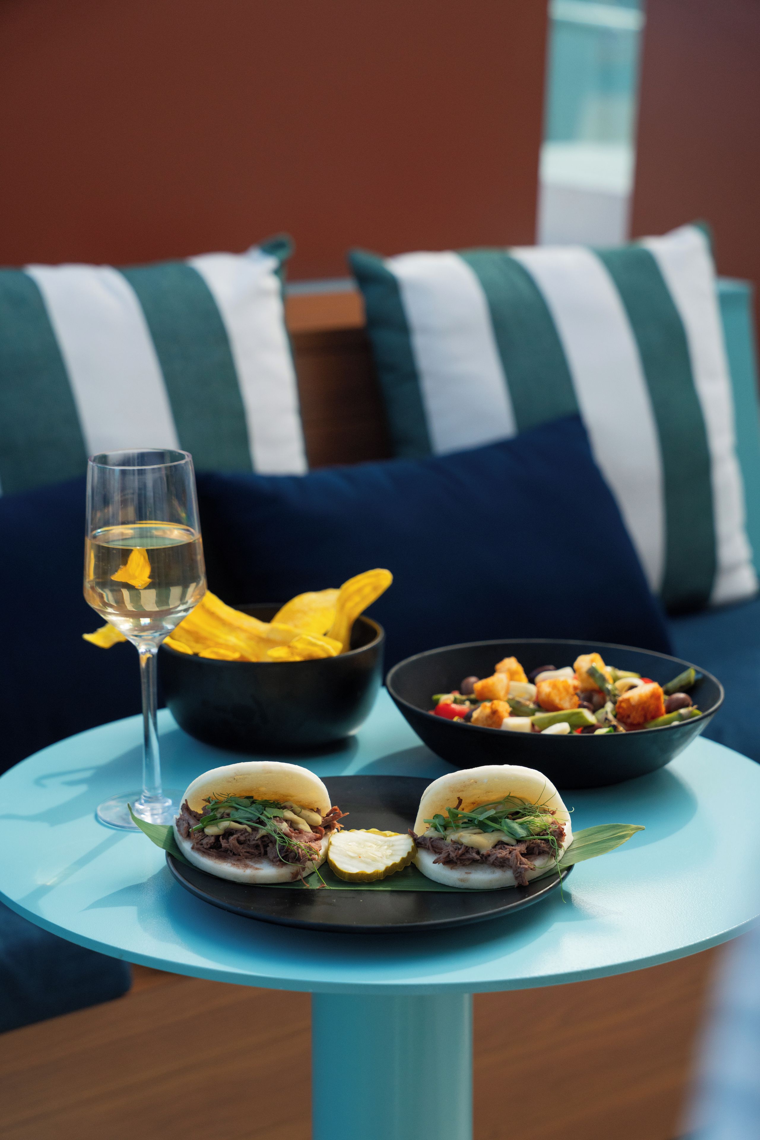 Una mesa con una copa de vino, dos fuentes de comida y un sándwich.