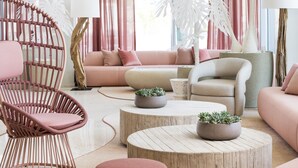 Una sala de estar moderna con un sofá rosa, una silla de mimbre y una mesa de centro redonda.