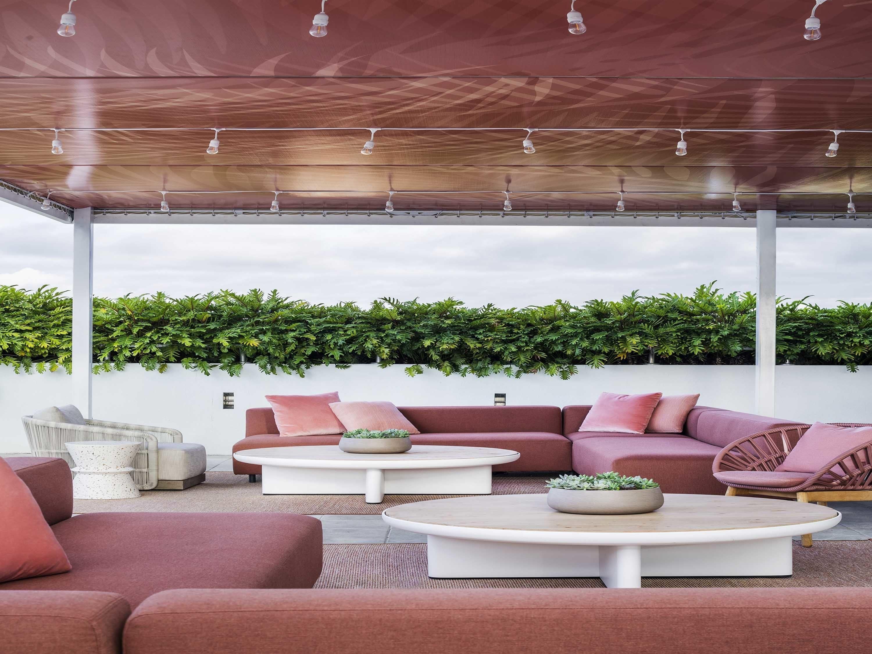 An outdoor seating area with a wooden ceiling, white walls, and green foliage.