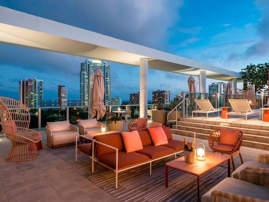 A rooftop lounge with outdoor seating, a staircase, and a city view at dusk.