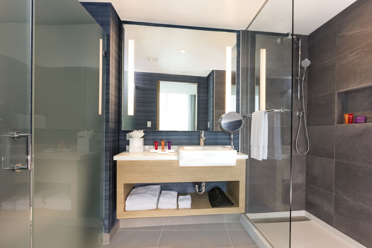 Un baño moderno con ducha envuelta en vidrio, tocador de madera y un espejo grande.