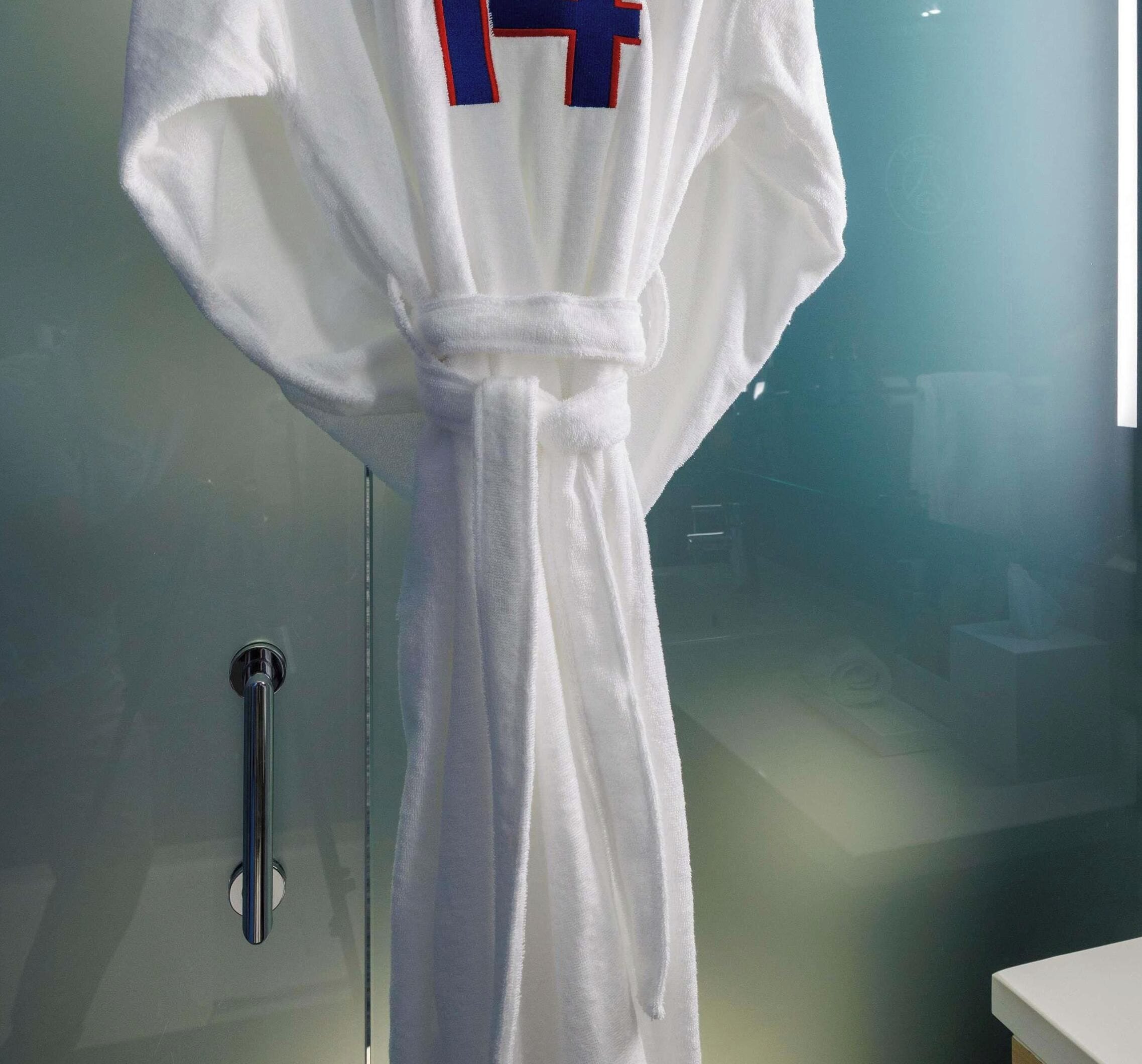 A white bathrobe hanging on a glass door.