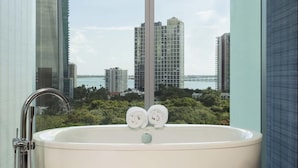Un baño con bañera, ducha y vistas a edificios altos y agua.