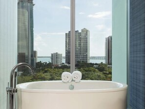 A bathroom with a bathtub, a shower, and a view of tall buildings and water.
