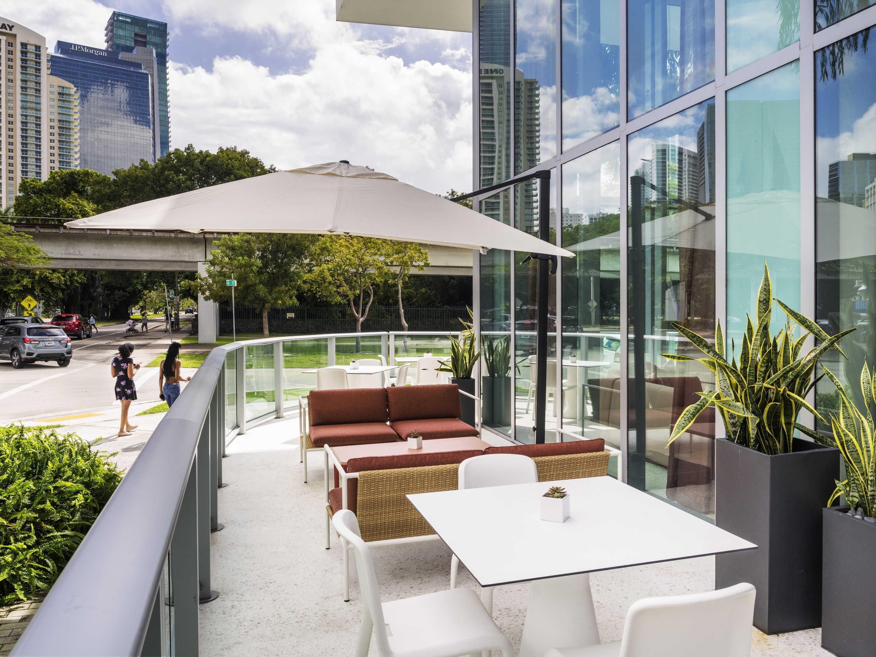 An outdoor patio with seating, a glass railing, and a view of the cityscape.