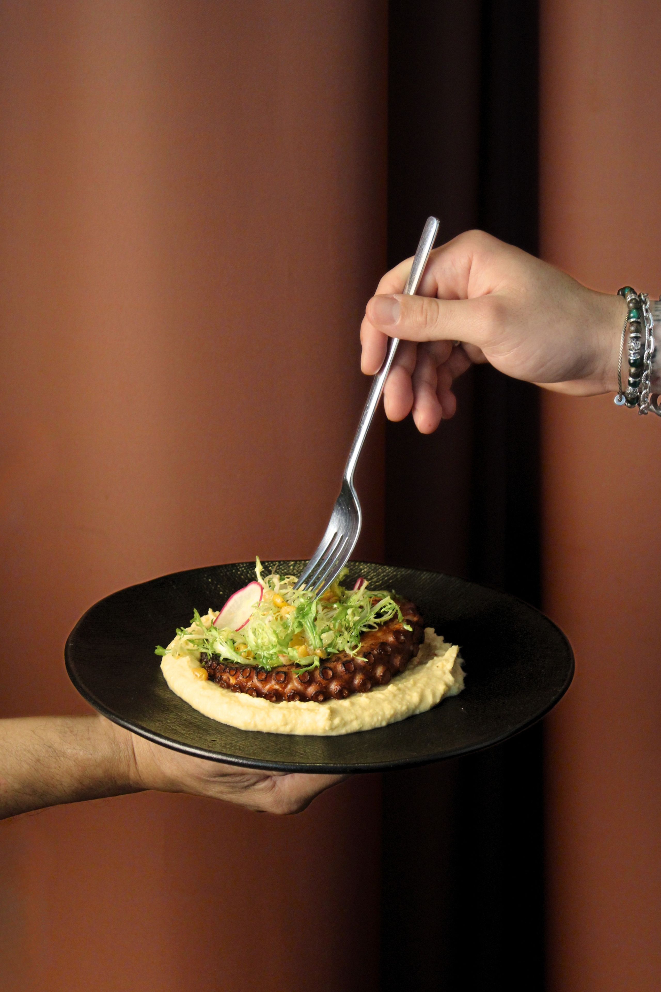 A person holding a plate with a food item, a fork, and a hand with a bracelet.