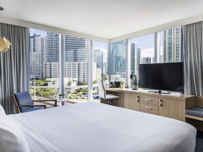 A hotel room with a large bed, a desk with a television, and a view of tall buildings. - Novotel Miami Brickell (Miami)