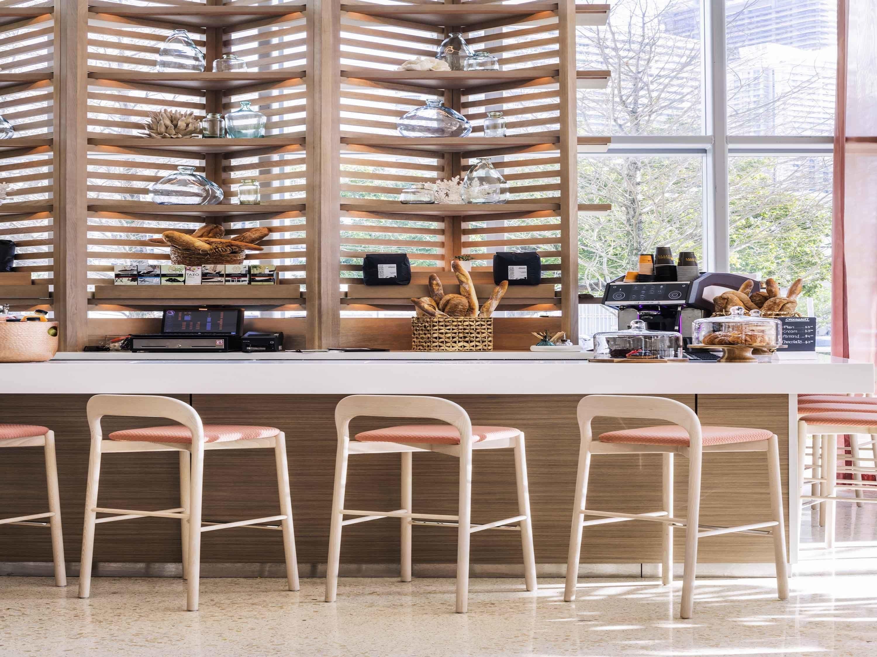 A café with a wooden slatted wall, a counter with a coffee machine, and three bar stools.