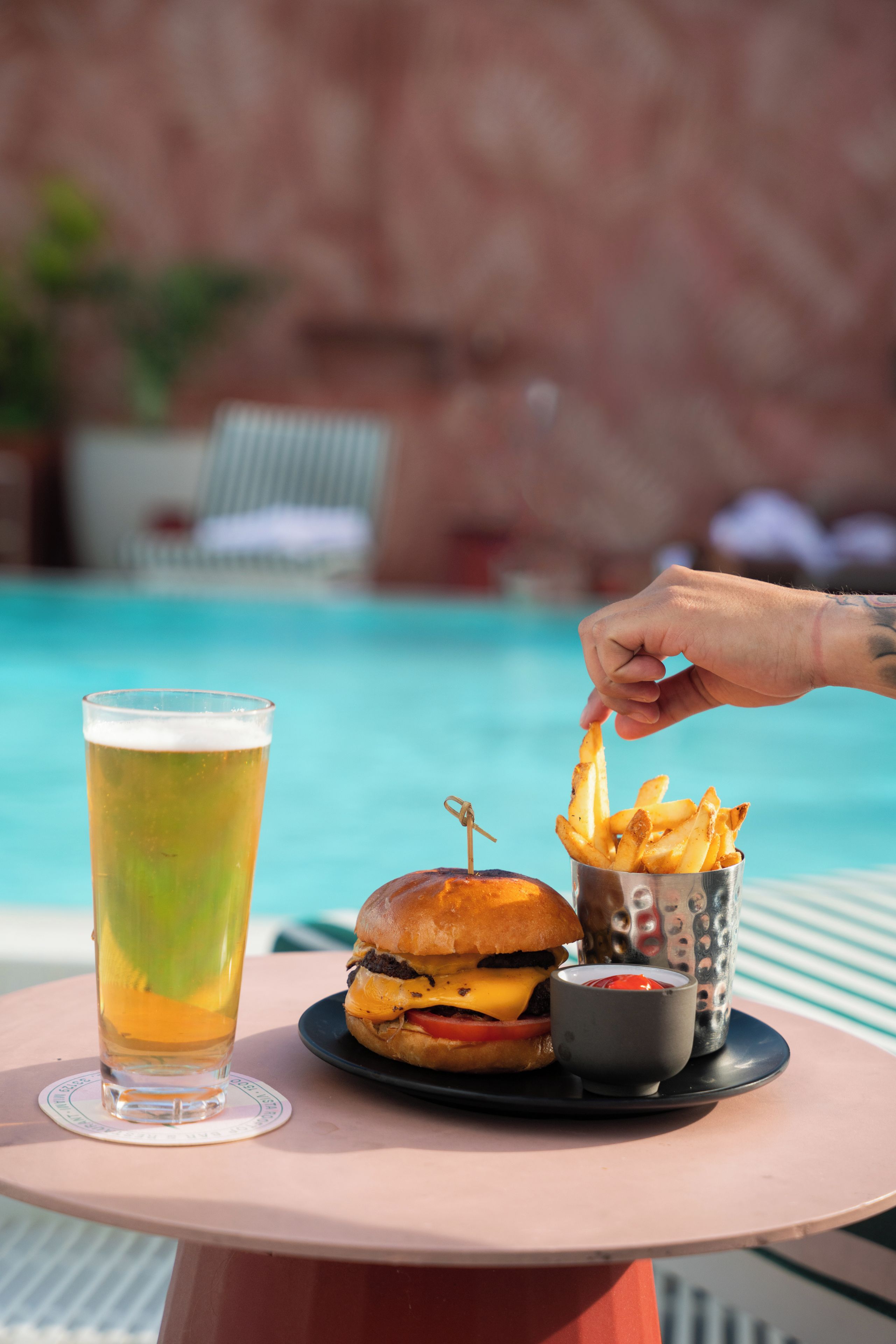 Eine Mahlzeit bestehend aus einem Burger, Pommes und einem Getränk, platziert an einem Tisch am Pool.