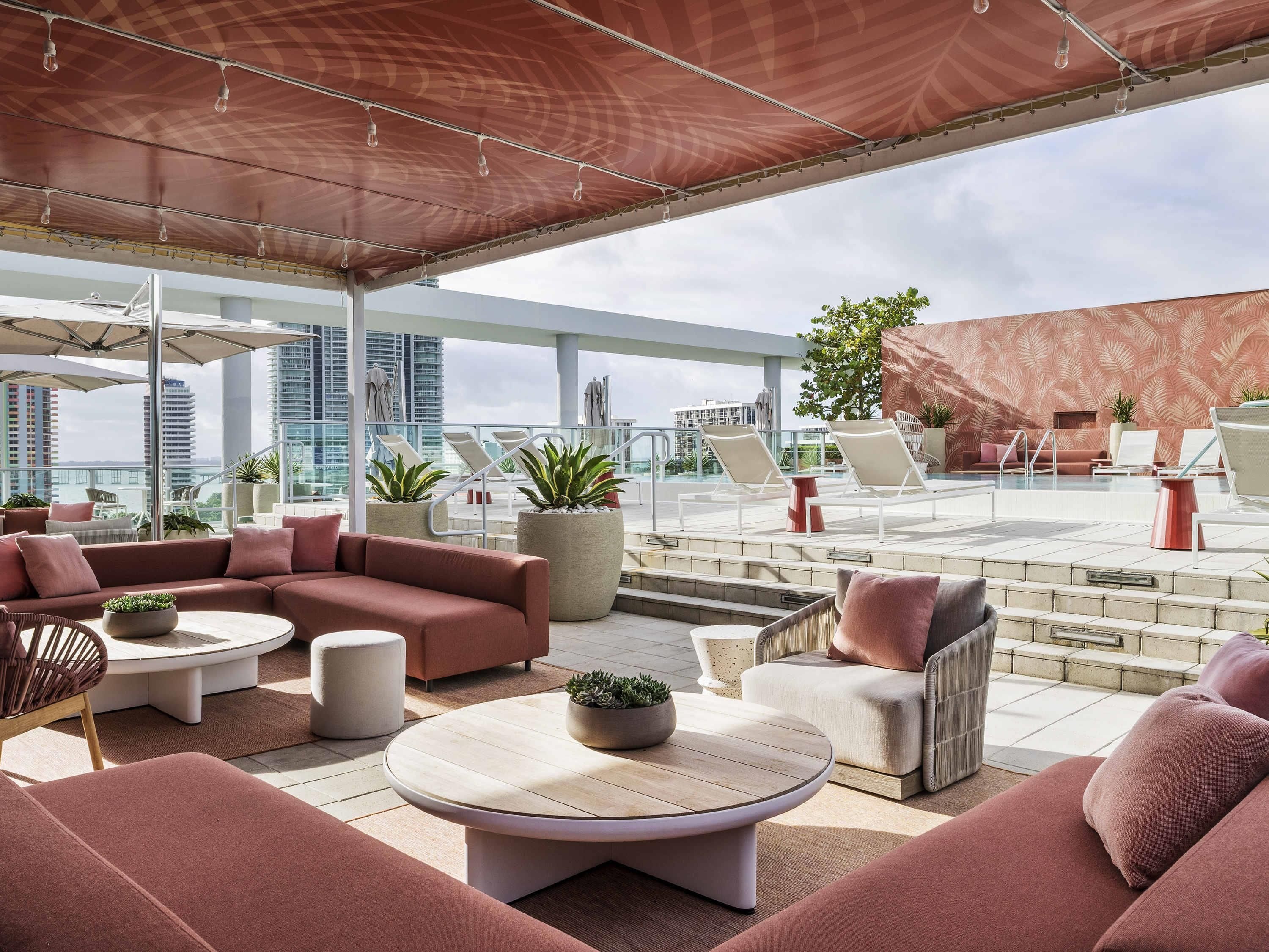 A rooftop lounge with outdoor seating, potted plants, and a view of the city skyline.