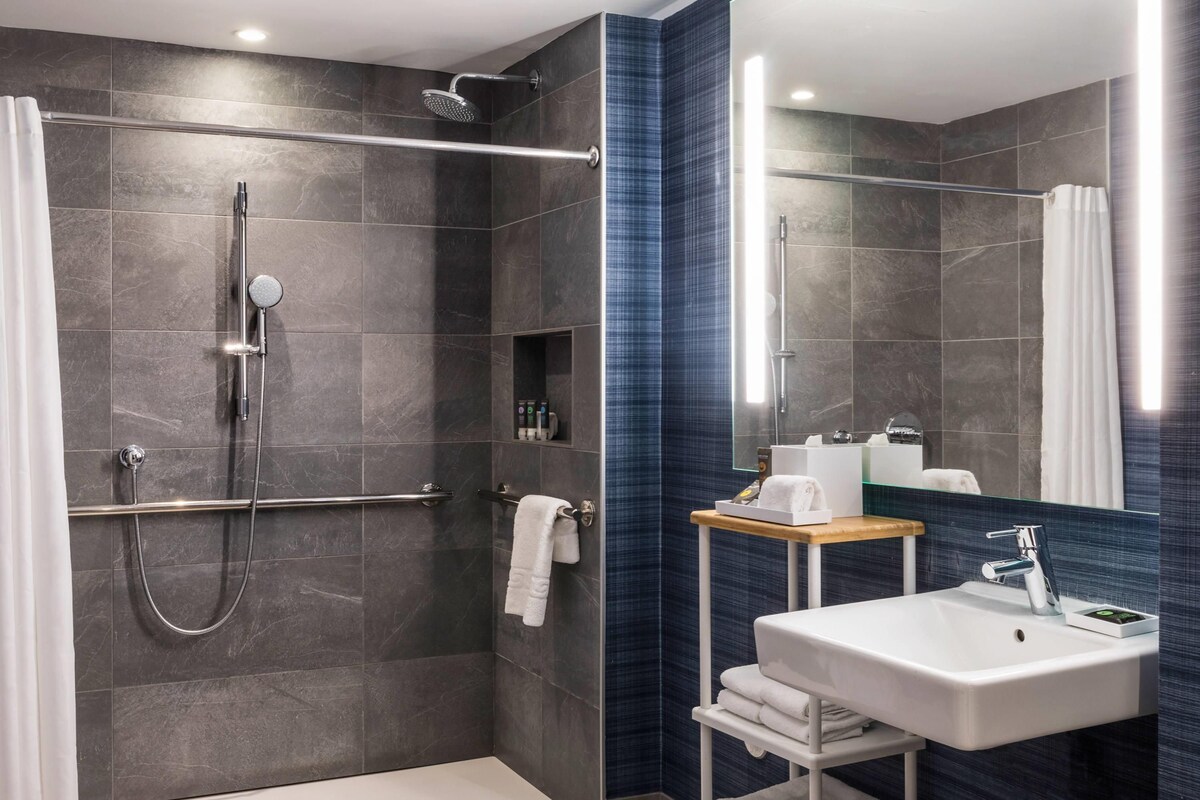 Un baño moderno con ducha a nivel, tocador con lavabo y espejo.