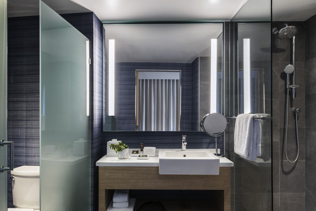 Un baño moderno con ducha envuelta en vidrio, un lavamanos blanco y un espejo grande.